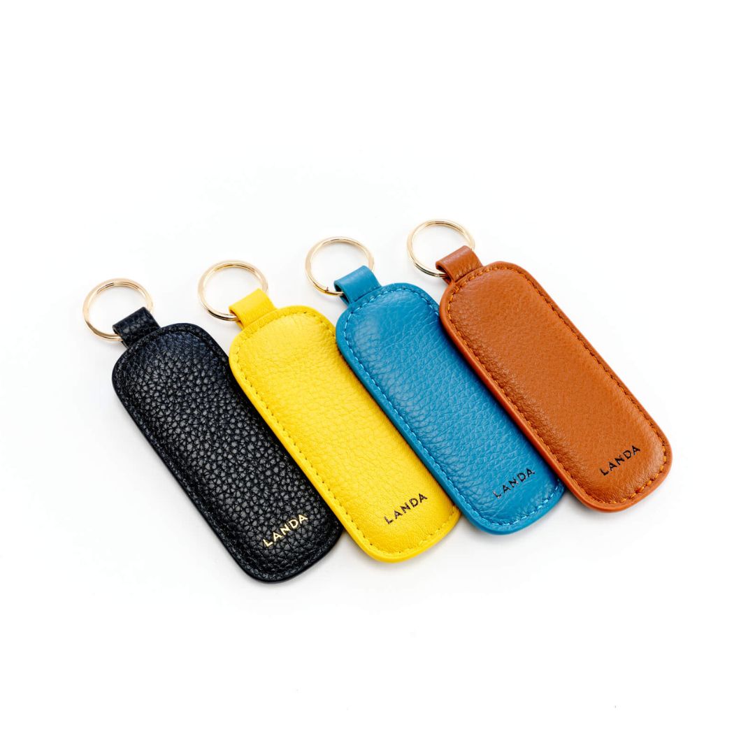 A collection of four leather key rings in black, blue, yellow, and tan, each with a gold-toned key ring attachment.