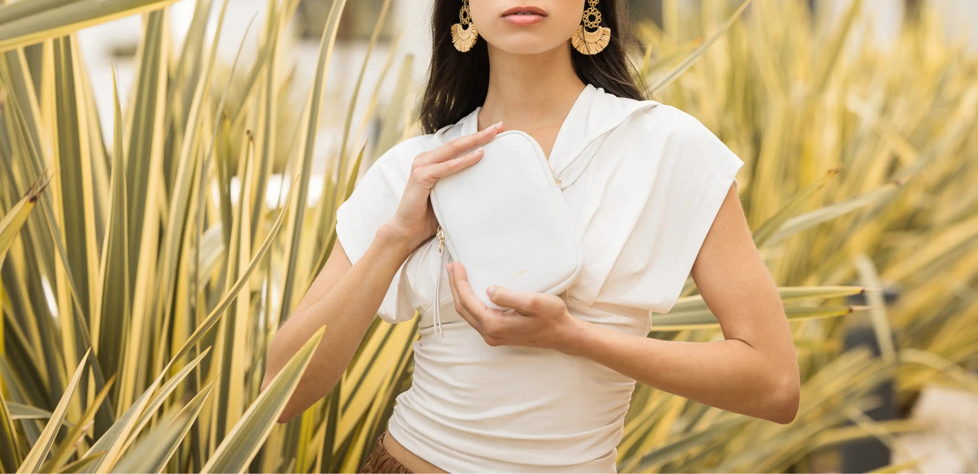 Woman holding a white leather phone bag in front of plants