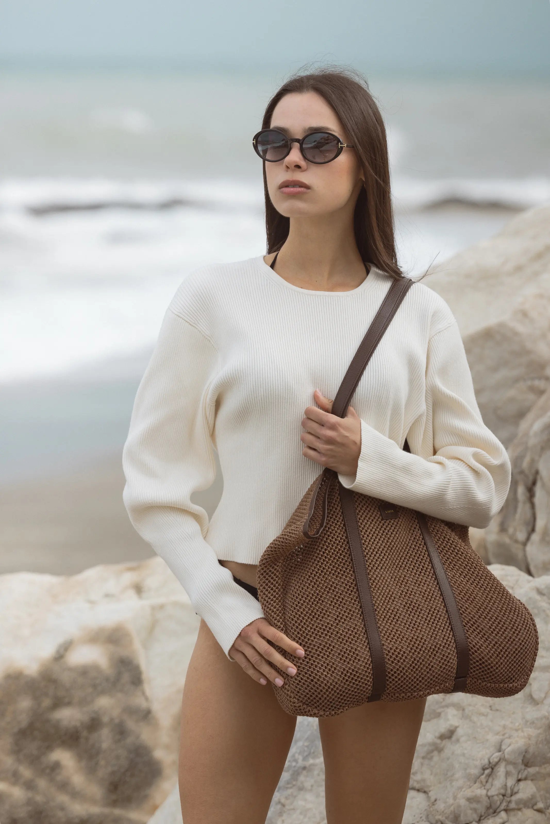 Woman holding a brown woven beach bag on a beach