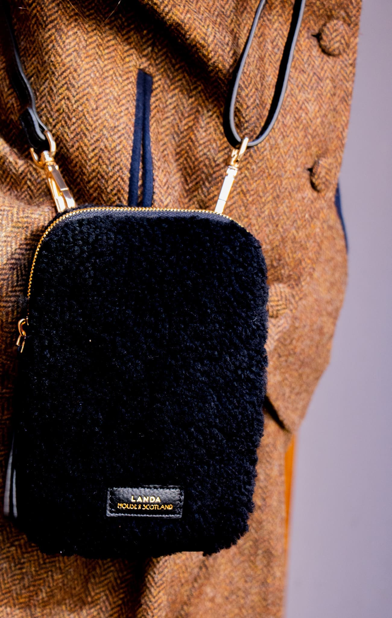 Black shearling pouch with gold zipper on a brown textured background