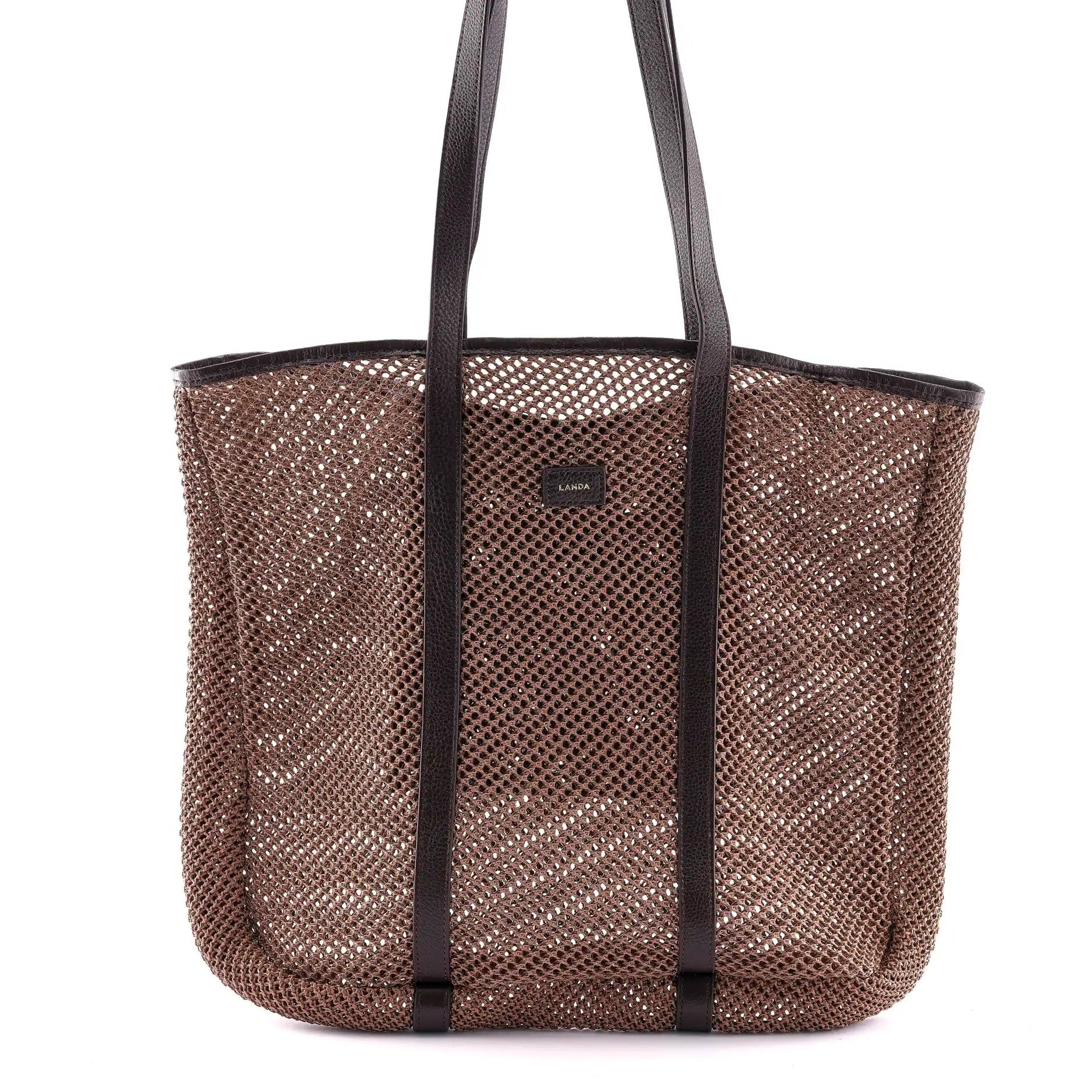 Brown woven beach bag with dark brown leather handles on a white background